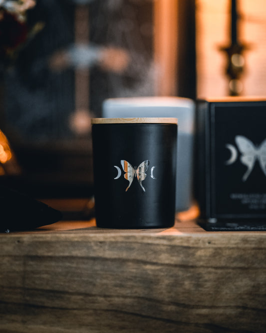 soy wax candle with matte black base and gold foil design of luna moth and crescent moons. Vetiver, cedar, and citrus.