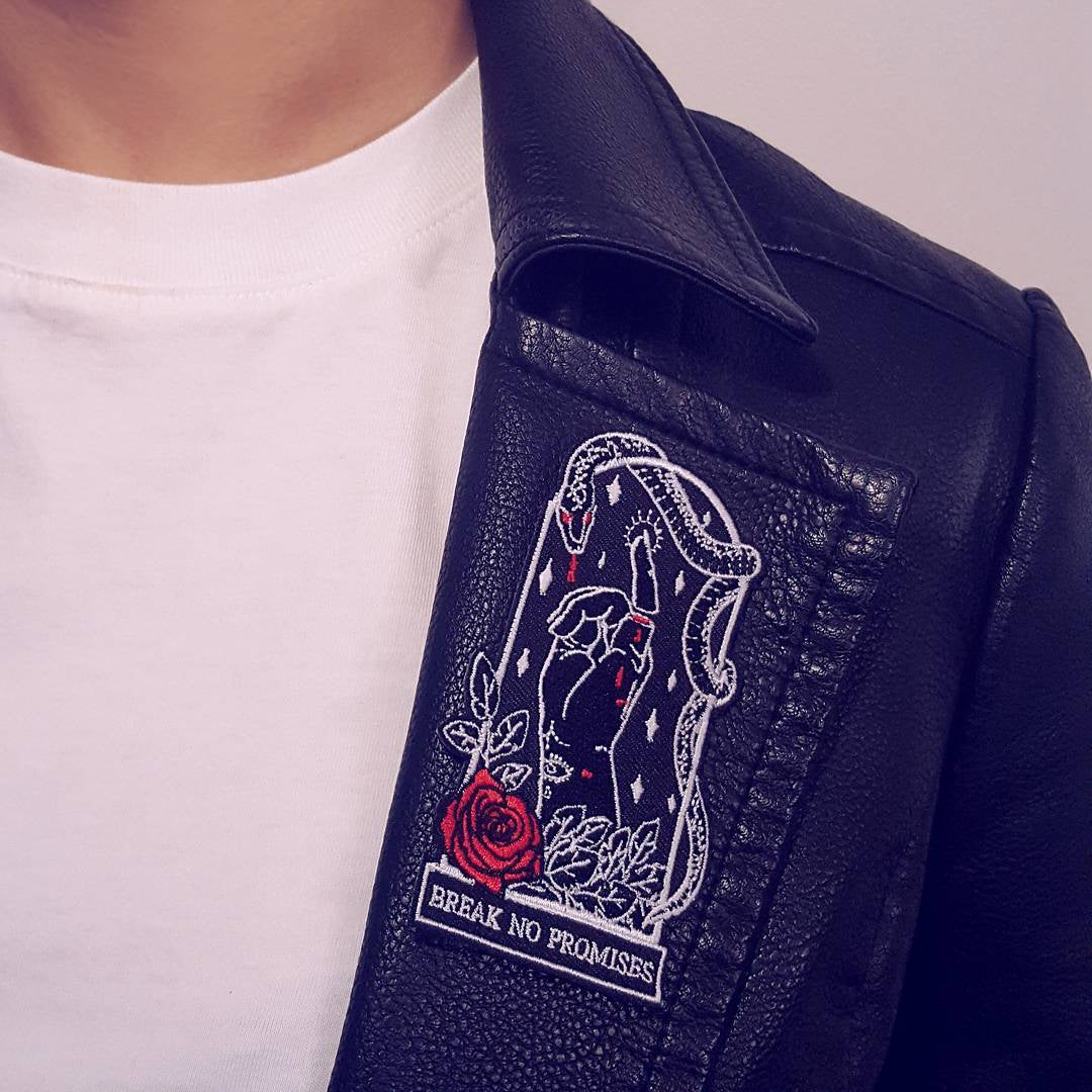 2.5"Wx4"H coffin-shaped embroidered patch featuring an iron-on backing. Patch reads "break no promises." We recommend that you apply a few stitches so the corners do not lift. Designed by Amrit Brar, produced by 13th Press. Embroidered patch, iron-on patch, denim patch, leather patch, biker patch, punk patch