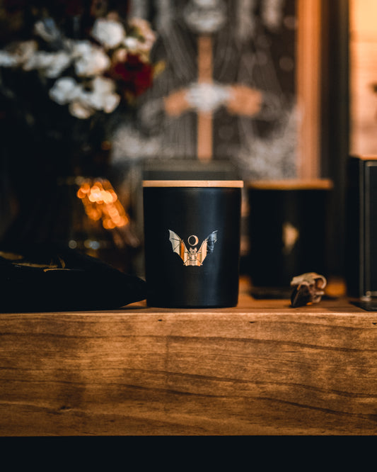 soy wax candle with matte black base and gold foil design of bat and crescent moon. T'erre de hermes.
