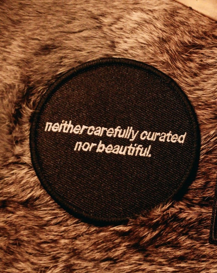 black and white machine embroidered iron-on patch that reads "neither carefully curated nor beautiful" designed by Amrit Brar and 13th Press