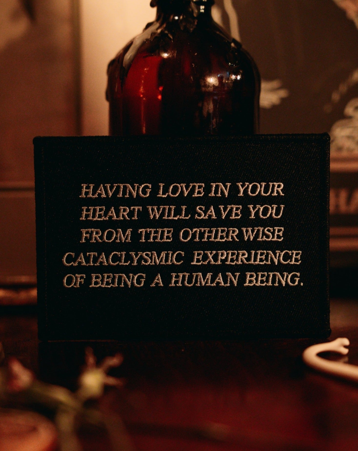 black and white embroidered iron-on patch designed by Amrit Brar and 13th Press. Text reads "having love in your heart will save you from the otherwise cataclysmic experience of being a human being"