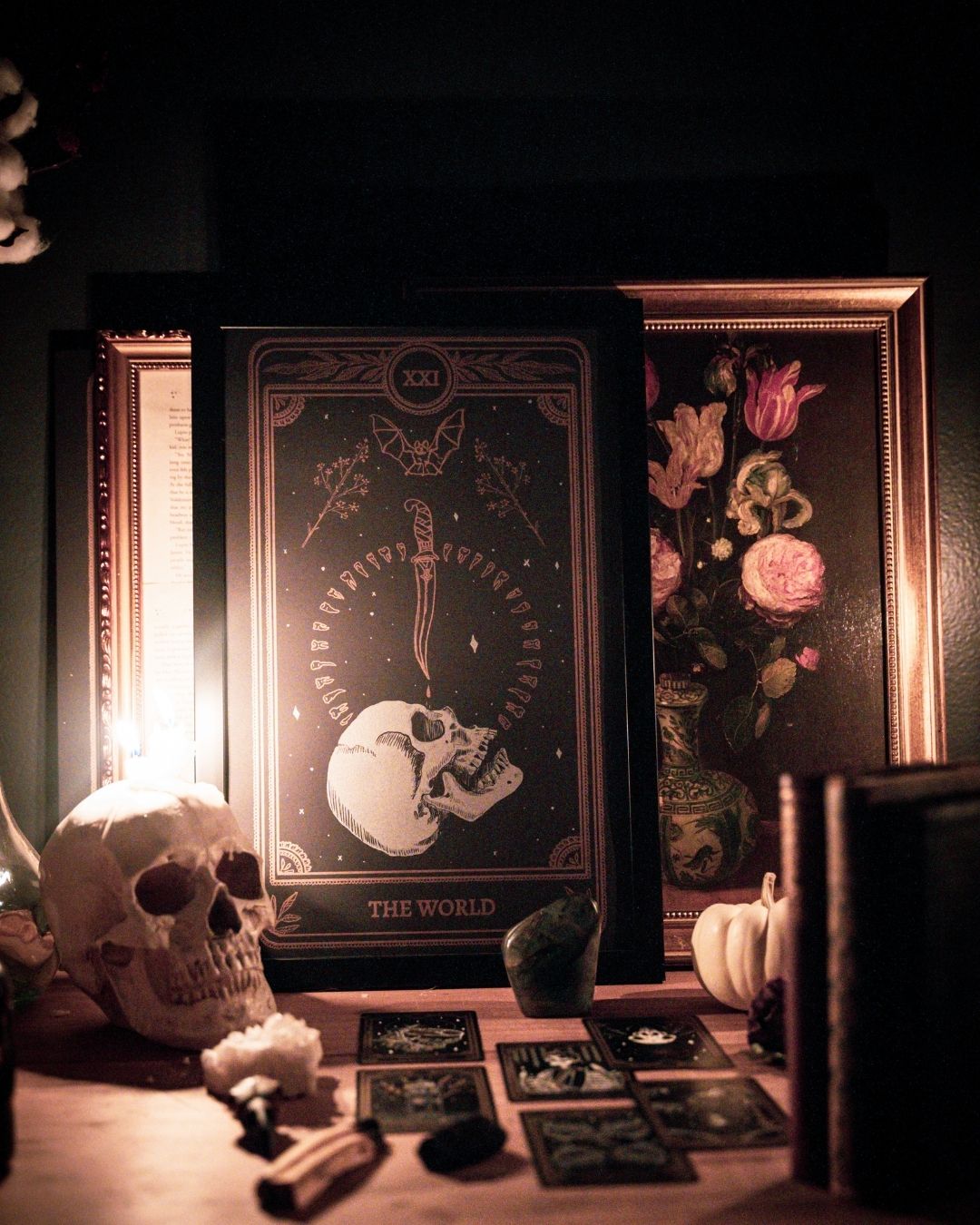 tarot card art print of the World tarot card from the Marigold Tarot deck by Amrit Brar and 13th Press. Candle light and eucalyptus foliage in the background. Black paper with white and bronze gold ink. Skull design with knife and bat.