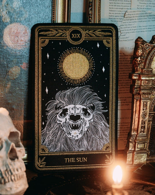 large embroidered patch of sun tarot card design from the Marigold Tarot deck by Amrit Brar and 13th Press. Skeleton of lion figure with sun and stars.