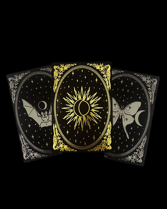 Three black notebooks with gold and gunmetal foil designs of a sun, moon, and luna moth on a black background.