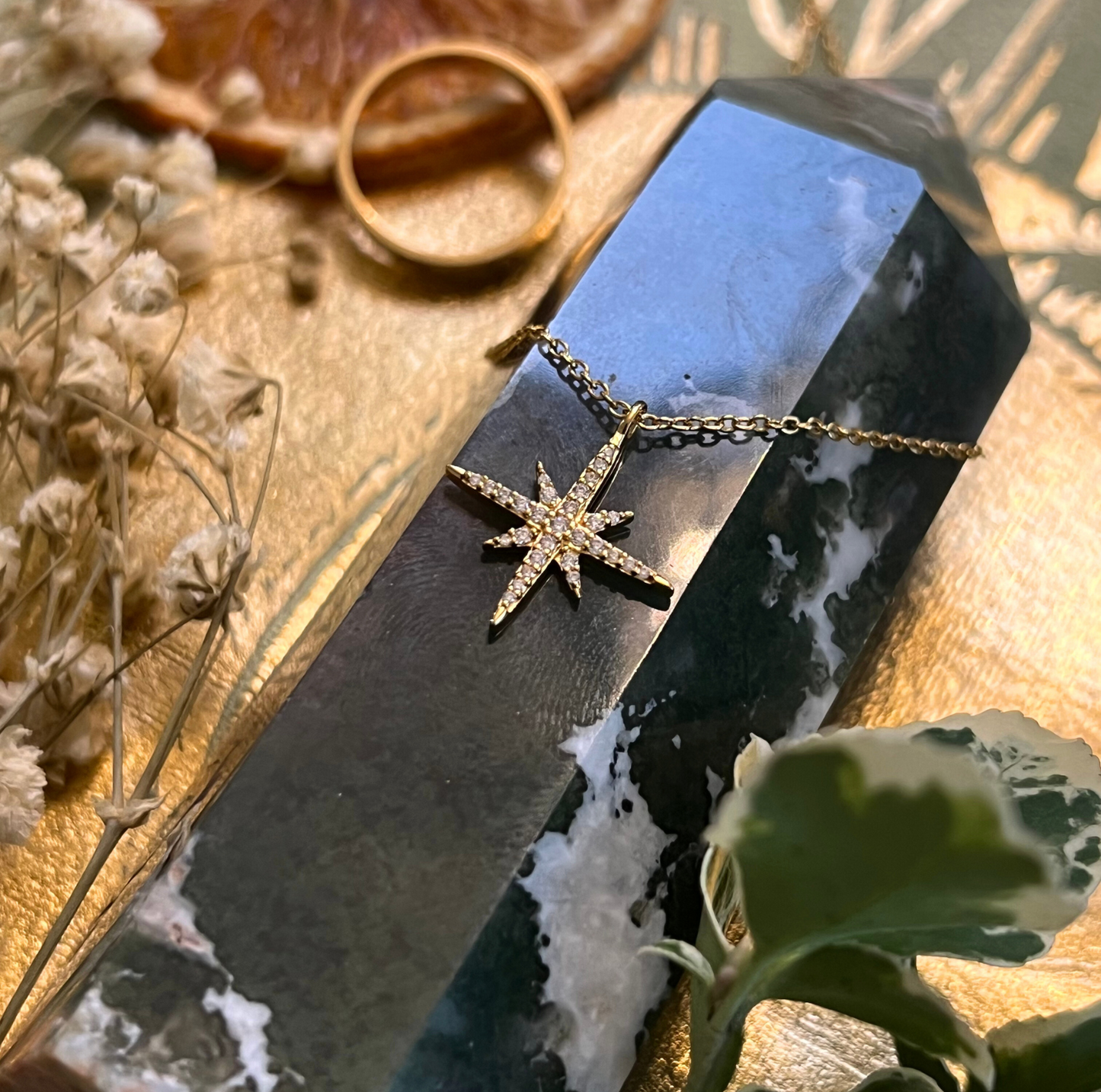 Star-shaped necklace on a dark stone with dried flowers and leaves in the background