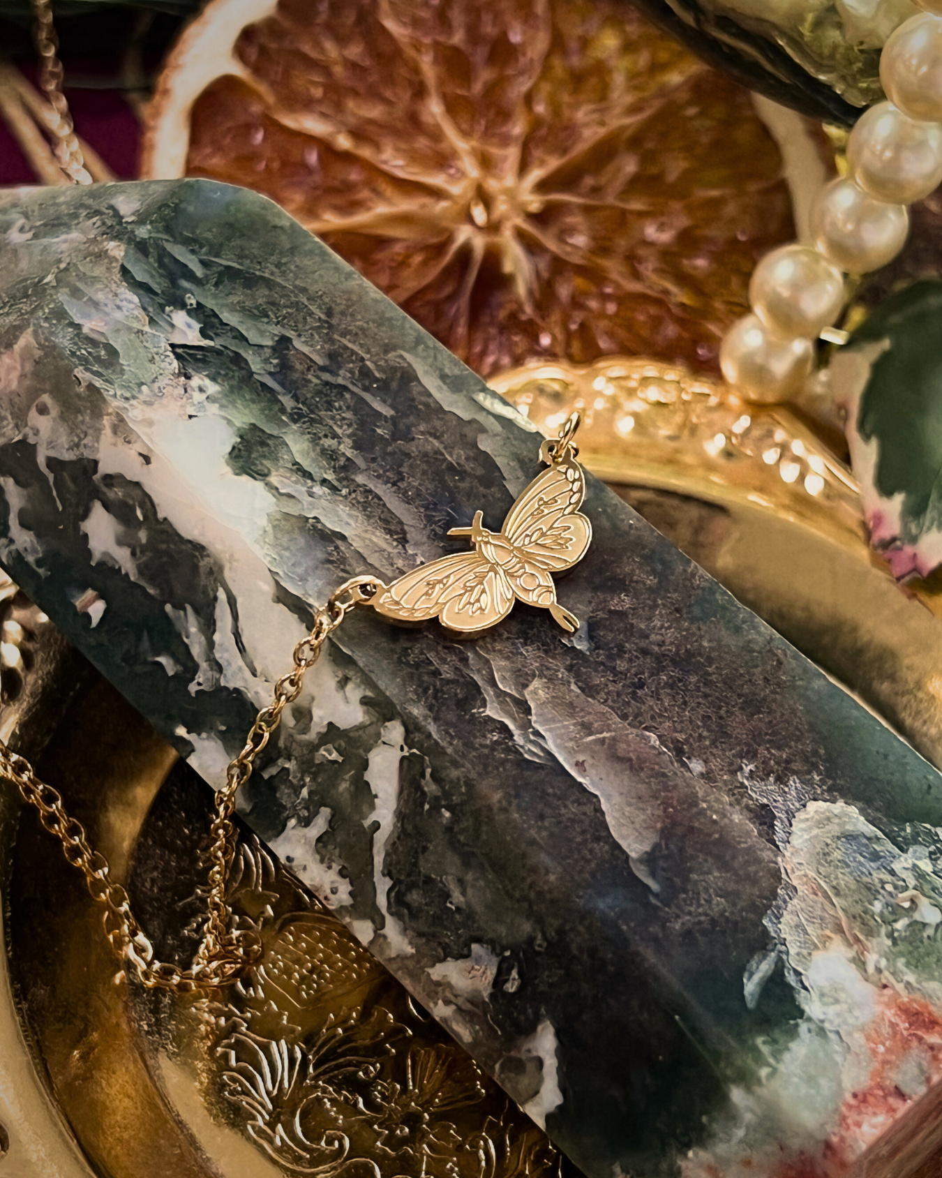 Gold butterfly pendant on a chain against a decorative background with dried fruit and pearls.