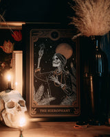 Hierophant print from the Marigold Tarot deck by Amrit Brar and 13th Press on altar stand with skull and candle. Black art print with gold and white ink.