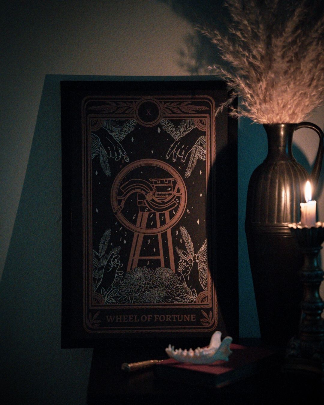 tarot card art print of the Wheel of Fortune card from the Marigold Tarot deck by Amrit Brar and 13th Press. With lit candle, vase and foliage. Skeleton jaw in front.