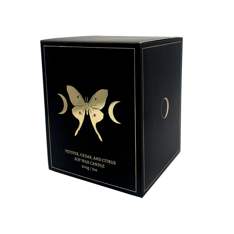 soy wax candle with matte black base and gold foil design of luna moth and crescent moons. Vetiver, cedar, and citrus.