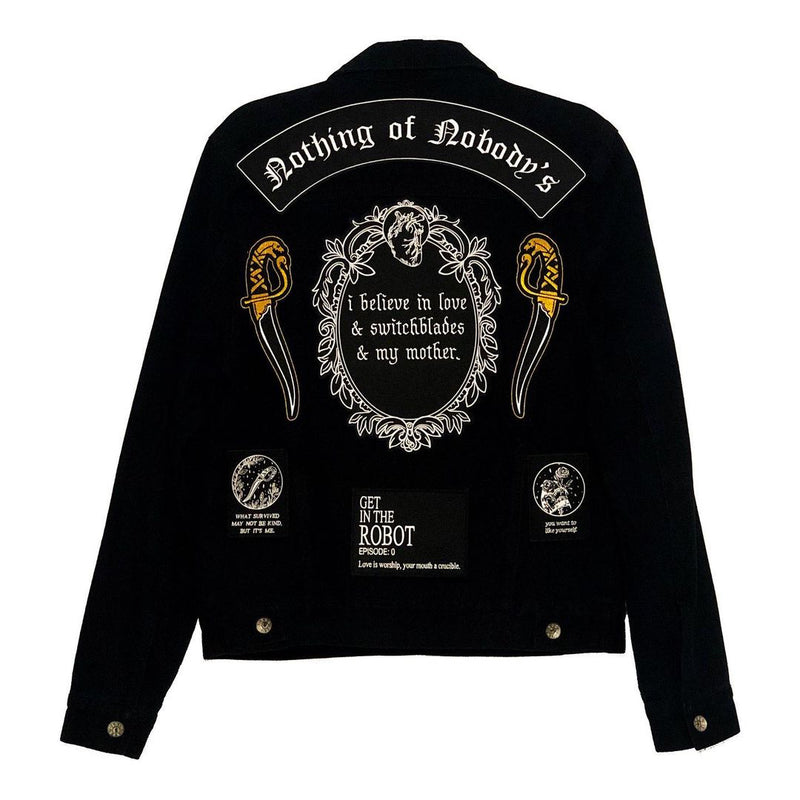 black and white iron-on embroidered back patch design from the Marigold Tarot deck by Amrit Brar and 13th Press. Text reads "i believe in love, switchblades, and my mother". Patches on black denim jacket.