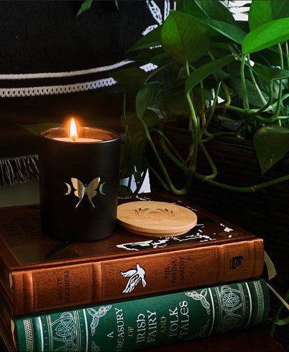 soy wax candle with matte black base and gold foil design of luna moth and crescent moons. Vetiver, cedar, and citrus.
