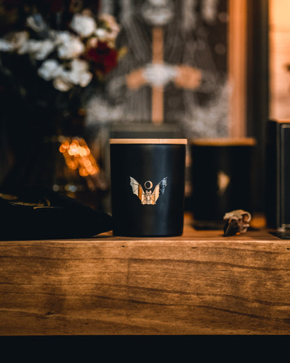 soy wax candle with matte black base and gold foil design of bat and crescent moon. T'erre de hermes.
