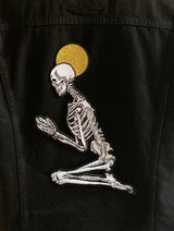 skeleton figure praying design of machine embroidered iron-on patch on back of black denim jacket