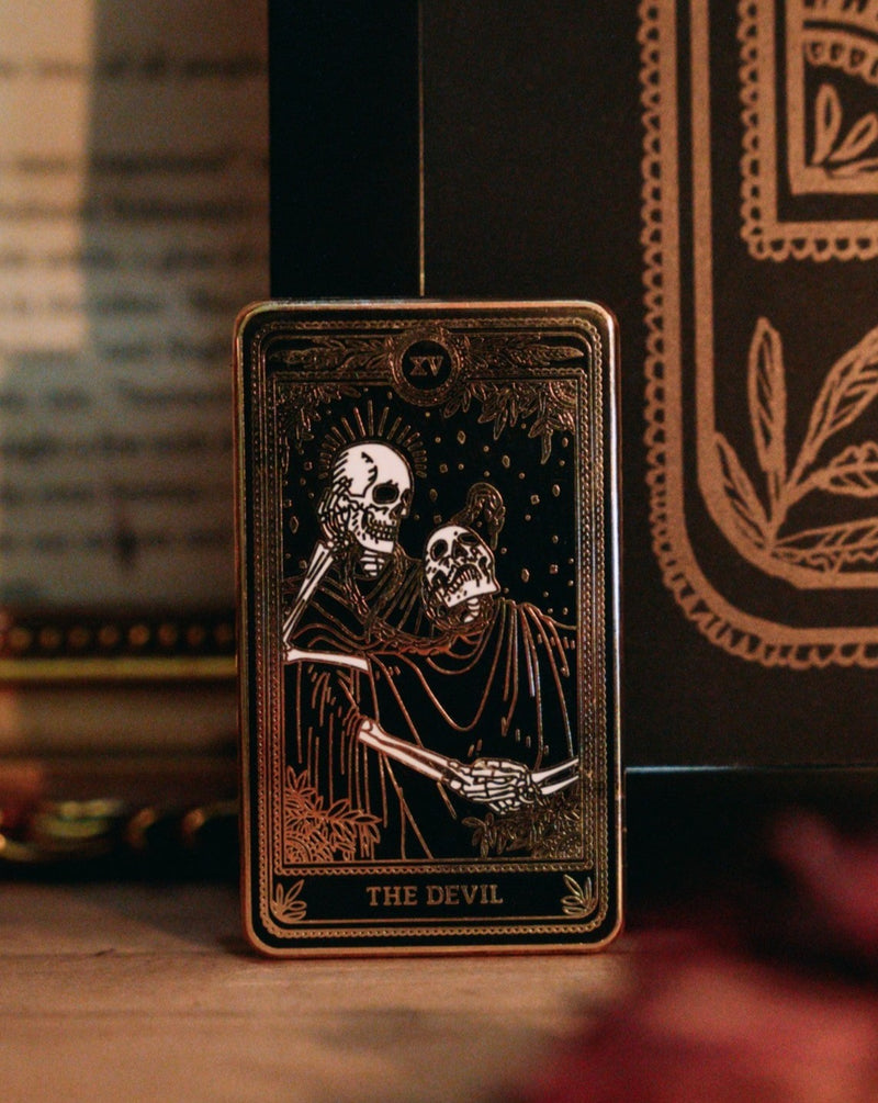 hard enamel pin, gold and black of the devil tarot card from the Marigold Tarot deck by Amrit Brar and 13th Press. Two skeletons and serpant
