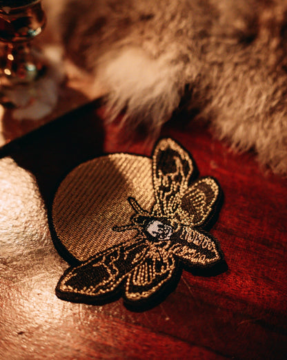 embroidered iron-on patch of moth and moon design by Amrit Brar and 13th Press. Machine embroidered with black, white, and gold thread.