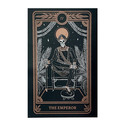 Emperor print with artwork from the Marigold Tarot deck by Amrit Brar and 13th Press on altar stand with foliage and candle light. Black print with white and gold ink of skeleton figure on throne.