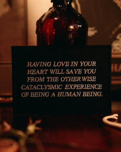 black and white embroidered iron-on patch designed by Amrit Brar and 13th Press. Text reads "having love in your heart will save you from the otherwise cataclysmic experience of being a human being"