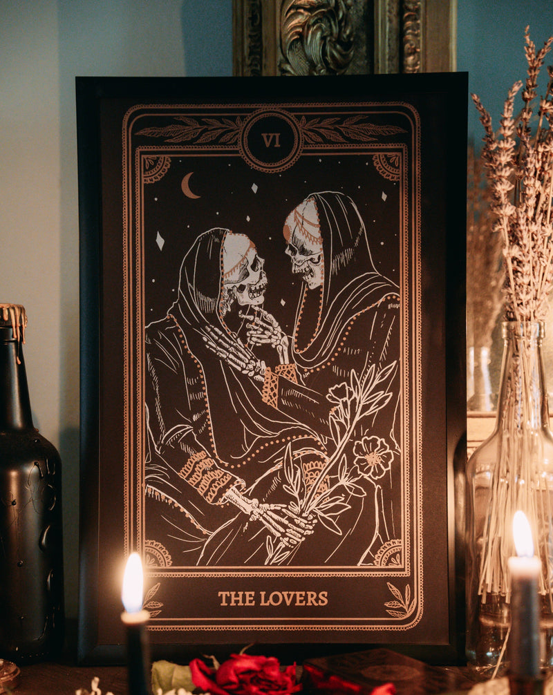 art print of the Lovers card from the Marigold Tarot deck by Amrit Brar and 13th Press on altar stand with lit candles and tarot card spread. Art of two skeletons embracing with flowers.