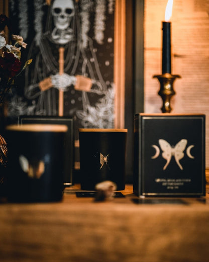 soy wax candle with matte black base and gold foil design of luna moth and crescent moons. Vetiver, cedar, and citrus.
