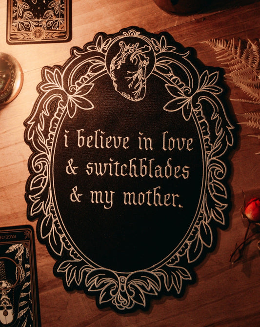 black and white iron-on embroidered back patch design from the Marigold Tarot deck by Amrit Brar and 13th Press. Text reads "i believe in love, switchblades, and my mother"