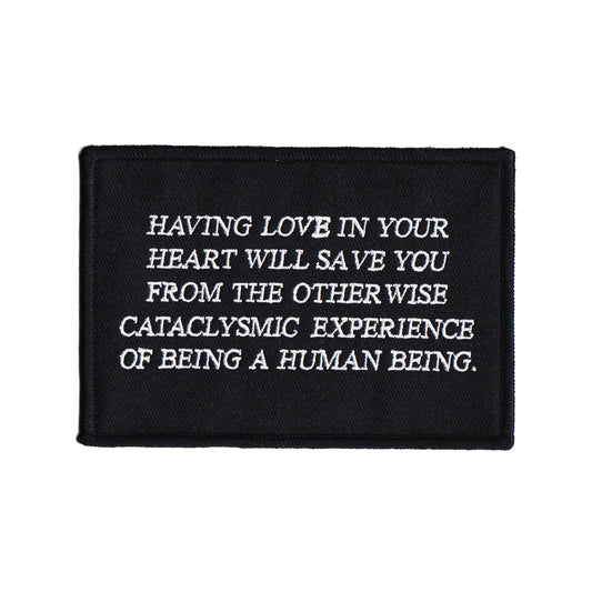 black and white embroidered iron-on patch designed by Amrit Brar and 13th Press. Text reads "having love in your heart will save you from the otherwise cataclysmic experience of being a human being"