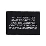black and white embroidered iron-on patch designed by Amrit Brar and 13th Press. Text reads "having love in your heart will save you from the otherwise cataclysmic experience of being a human being"