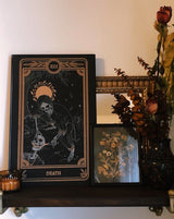 Tarot Death print from the Marigold Tarot Deck and Tarot stand by Amrit Brar and 13th Press on Altar and includes foliage. Skeleton art