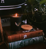 soy wax candle with matte black base and gold foil design of bat and crescent moon. T'erre de hermes scent. Displayed on altar with books and plants.