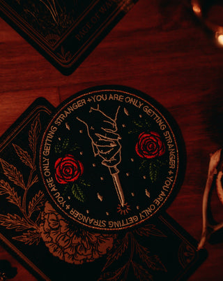 machine embroidered iron-on patch with knife and roses, text reads "you are only getting stranger" on green denim jacket with hard enamel pin of skeleton and rose.