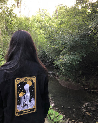 strength tarot card large embroidered back patch with black, gold, and white thread, design from the Marigold Tarot deck by Amrit Brar and 13th Press. Iron-on patch on black denim jacket.