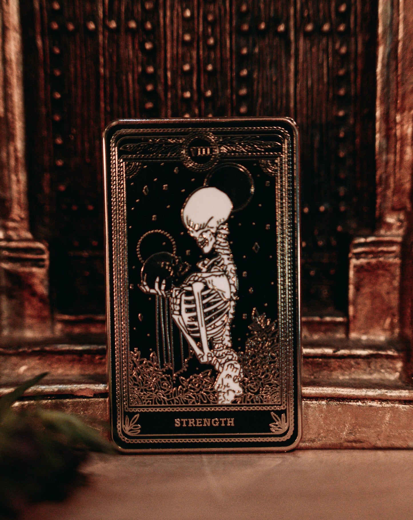 hard enamel pin of strength tarot card from the Marigold Tarot deck by Amrit Brar and 13th Press. Black pin with gold and white ink. Pin for jackets and bags
