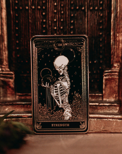 hard enamel pin of strength tarot card from the Marigold Tarot deck by Amrit Brar and 13th Press. Black pin with gold and white ink. Pin for jackets and bags