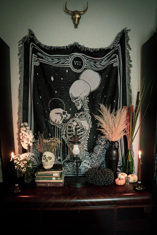 woven tapestry of the Strength tarot card from the Marigold Tarot deck by Amrit brar and 13th Press. Tapestry hung above altar stand with skull decor and dried flowers.