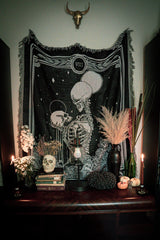 woven tapestry of the Strength tarot card from the Marigold Tarot deck by Amrit brar and 13th Press. Tapestry hung above altar stand with skull decor and dried flowers.
