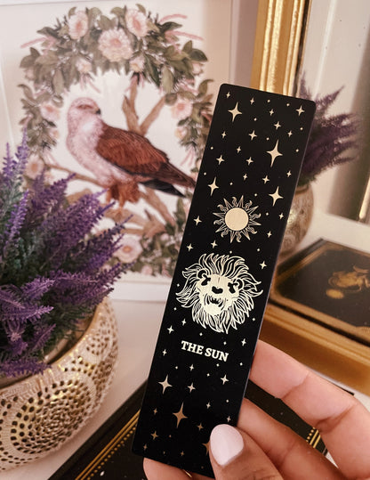 bookmark with the Sun tarot card design. Art from the Marigold tarot deck by Amrit Brar and 13th Press. Black and gold metal bookmark.