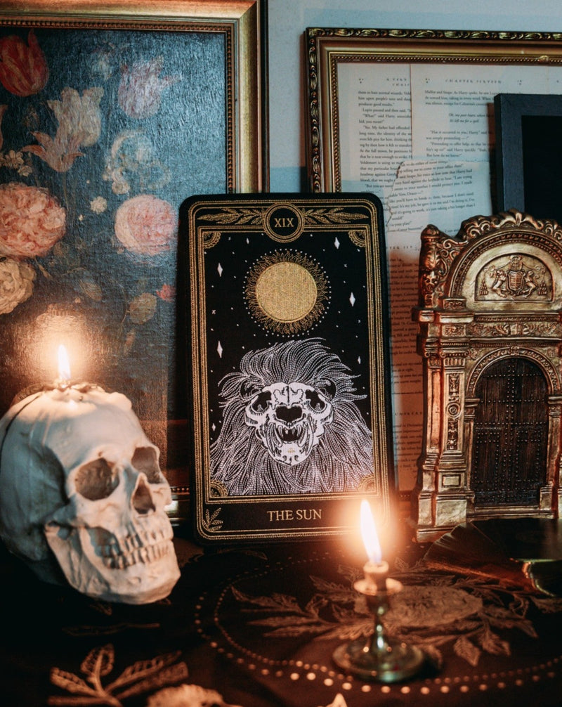 large embroidered patch of sun tarot card design from the Marigold Tarot deck by Amrit Brar and 13th Press. Skeleton of lion figure with sun and stars. Patch on table with tarot altar cloth, skull, and candle light.